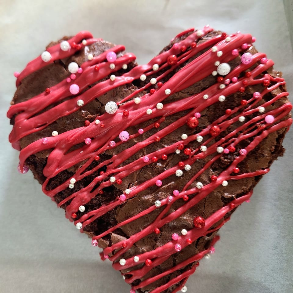 Heart-shaped brownie with red icing drizzle and pink, red, and white sprinkles.