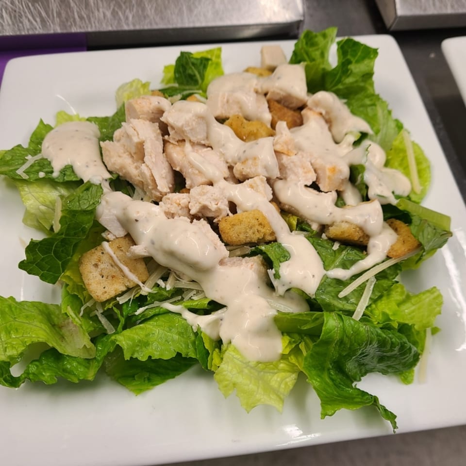 A Caesar salad with chicken, croutons, and dressing on a white rectangular plate.