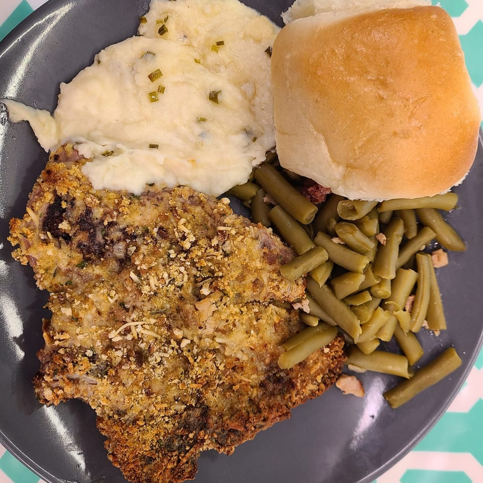 Breaded pork chop, mashed potatoes with chives, green beans, and a dinner roll on a gray plate.