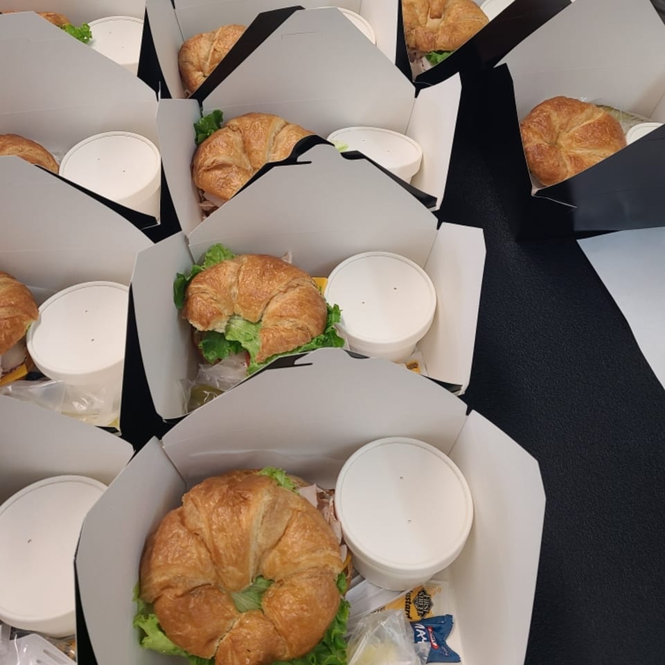Multiple catering boxes from Hollie's Hometown Kitchen, each with a croissant sandwich and side dish.