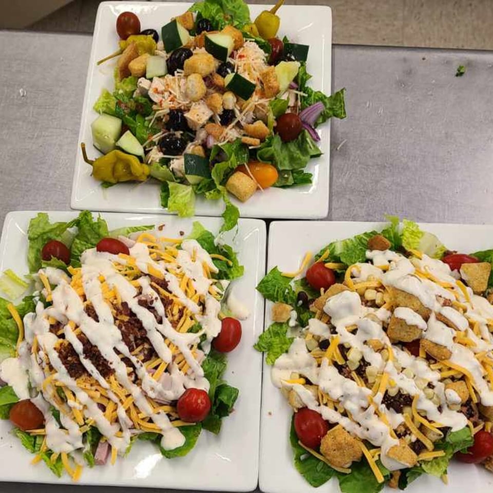 Three American-style salads with various toppings, including cheese, bacon, and dressing, on white plates.