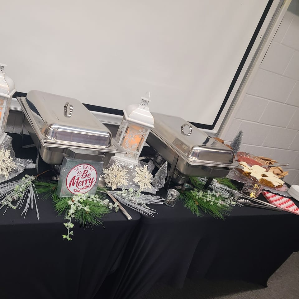 Hollie's Hometown Kitchen catering setup with chafing dishes, holiday decorations, and desserts on a black tablecloth.