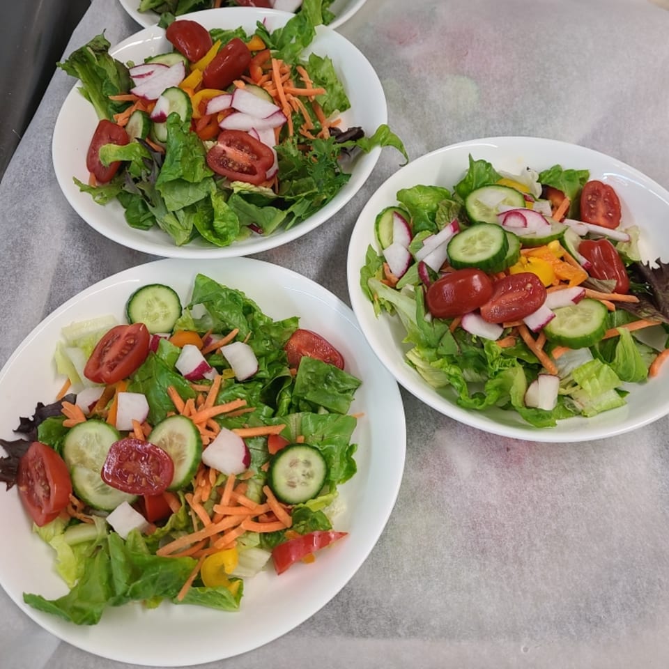Three white bowls of fresh green salad with tomatoes, cucumbers, radishes, and shredded carrots.
